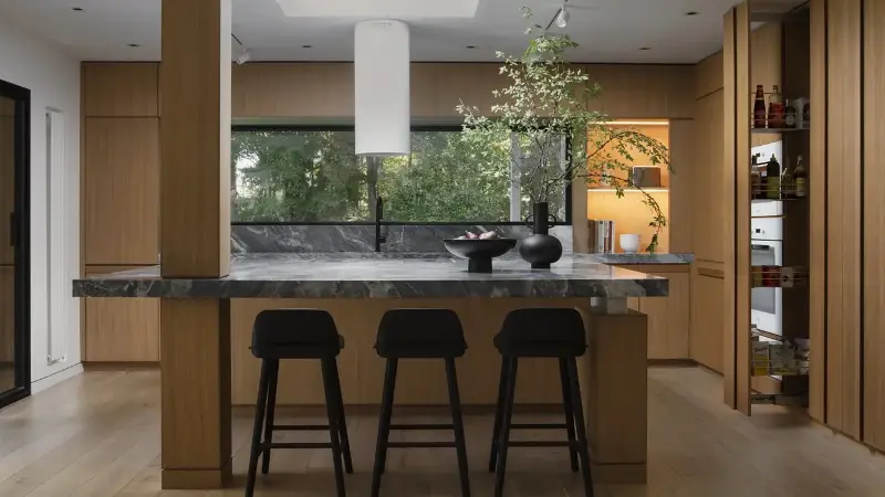 a wood kitchen with a stone topped kitchen island with a column running through