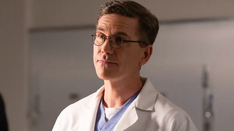 Jimmy talking about birthdays with Tony in the morgue. He's wearing a white lab coat and his signature wire-frame glasses.