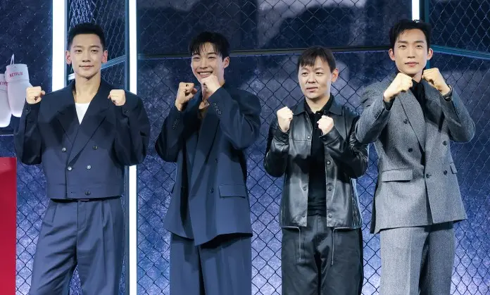 Bloodhounds cast standing in a promotional event, all dressed in formal attire, with two giving a fist pose and smiling.