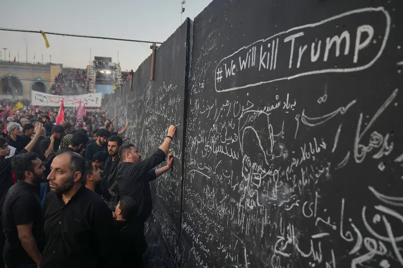Mourners write messages on a wall, including one in English that reads 