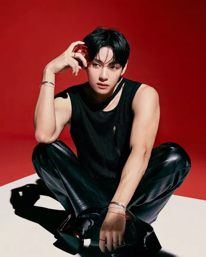 V sitting on a white surface against a red background, wearing a black sleeveless top and leather pants, holding TIRTIR cushion in one hand.