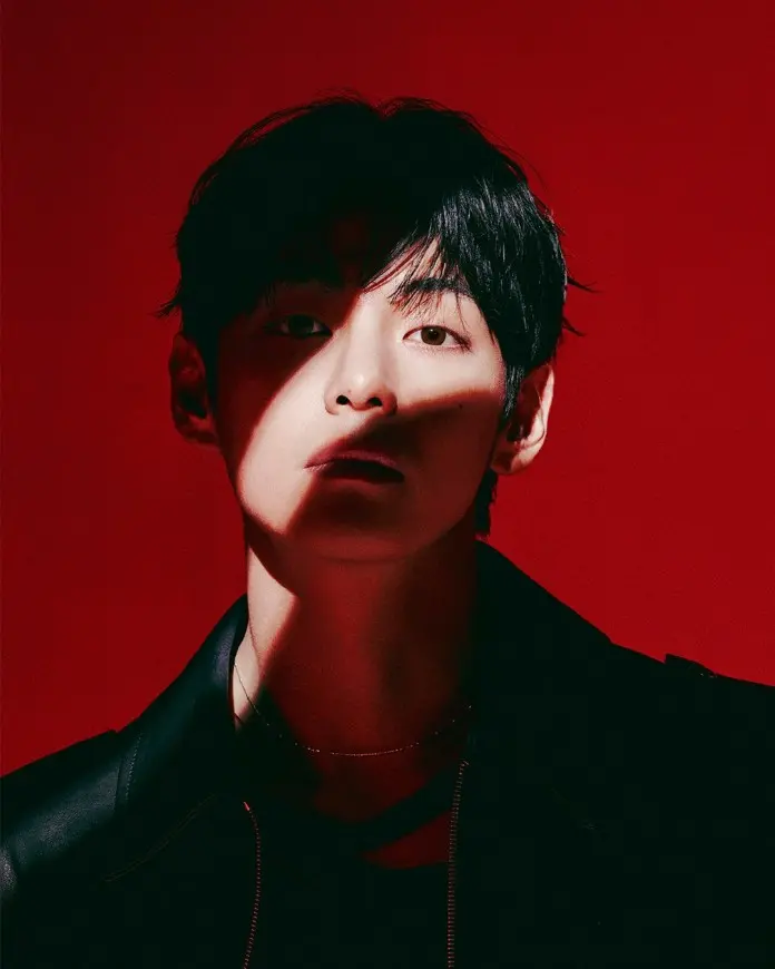 V with dark hair and a leather jacket, illuminated against a red background with dramatic shadows across their face.