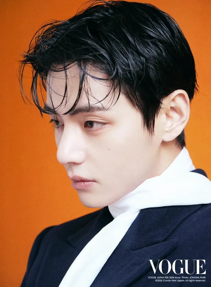 Close-up profile of V with dark, slicked-back hair, wearing a navy suit and white scarf, set against an orange background.
