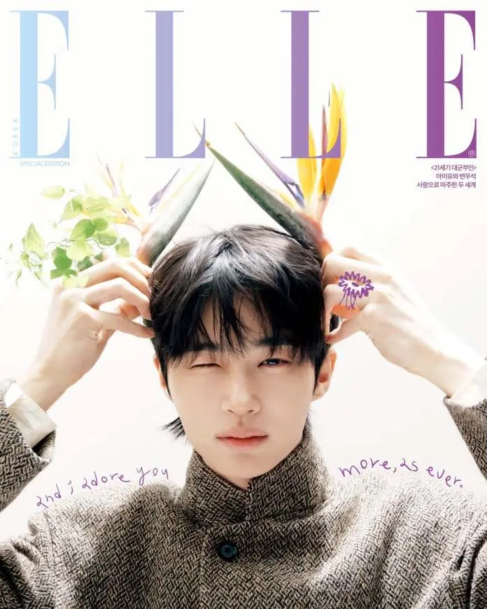 Byeon Woo-seok with dark hair wearing a textured sweater, playfully posing with hands on his head, adorned with bright, tropical plant elements. The magazine cover features the title 'ELLE' and a handwritten quote that reads 'and I adore you more, as ever.'
