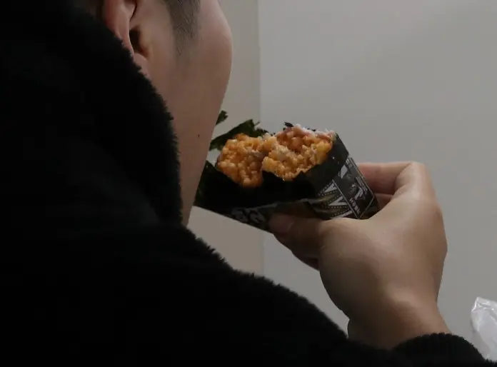 Person holding kimbap roll filled with rice and other ingredients, partially eaten.