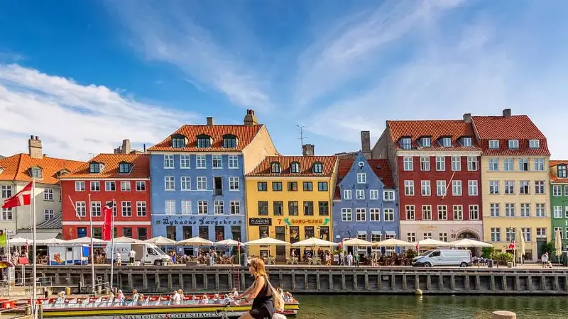 Copenhagen iconic view. Famous old Nyhavn port with colorful medieval houses, tourist ship and woman on a bicycle in the center of Copenhagen. Selective focus