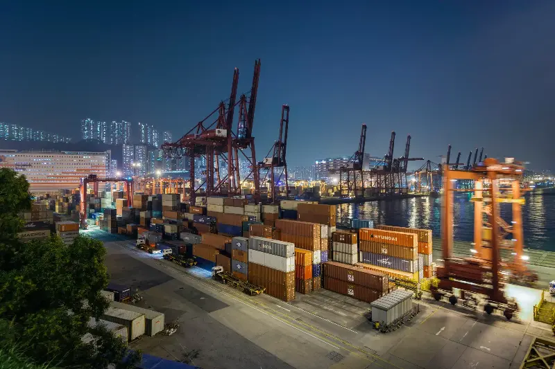 Asia, China, Hong Kong, cranes at the container port, showing fork lifts loading and unloading trucks transporting cargo containers, at dusk