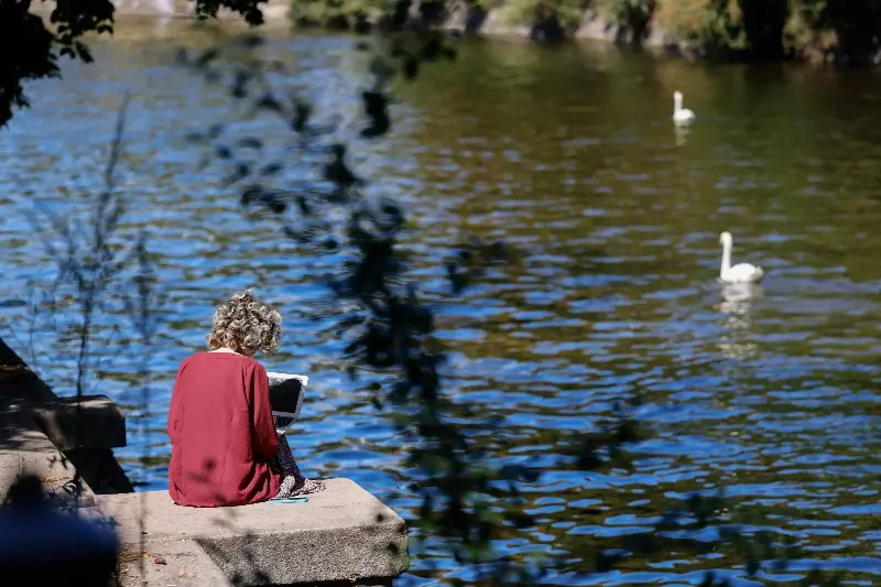 A woman uses a laptop as she sits on the banks of the Landwehr canal in Berlins Neukoelln district as the sun shines on July 24, 2022.