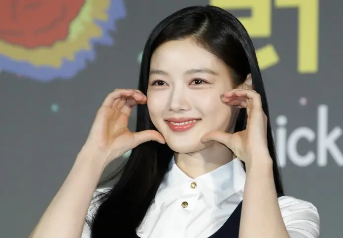 Kim Yoo-jung with long black hair is making a playful gesture by framing her face with her hands, set against a colorful background.