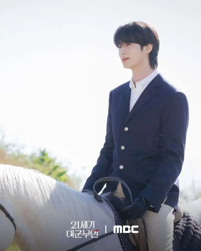 Byeon Woo-seok in a navy blazer and white shirt sits on a white horse, gazing thoughtfully into the distance against a bright sky.