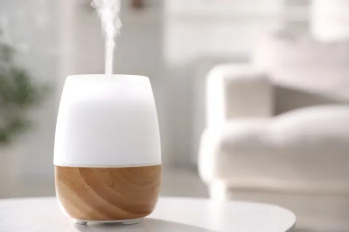 A white and wooden essential oil diffuser emitting mist, placed on a table with a soft background.