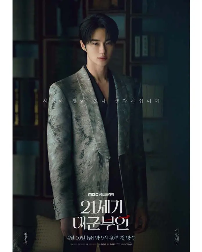 Byeon Woo-seok in a stylish patterned suit stands confidently, looking directly at the camera. The background features dark shelves with books, and text in Korean is featured prominently at the center of the image. The poster promotes the drama series Perfect Crown.