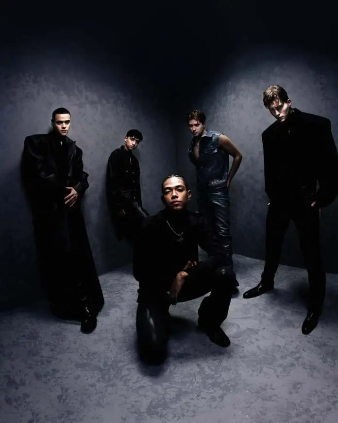 SANTOS BRAVOS members posing together in a dramatic and moody setting, wearing stylish black and denim outfits, with one member crouching in the foreground.