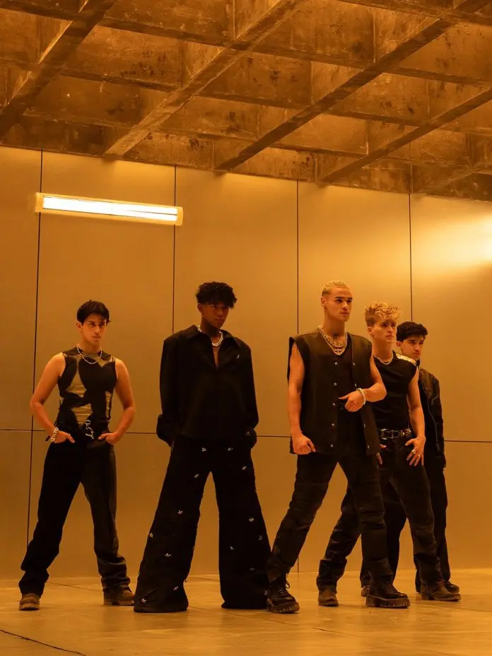 SANTOS BRAVOS members standing in a modern, illuminated room with concrete walls, showcasing diverse fashion choices.