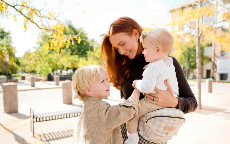 A mom holds her younger child on her Tushbaby hip carrier.