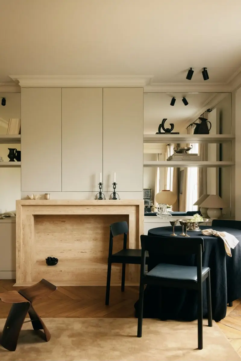This bespoke travertine fireplace anchors the room, while mirrored panels behind the built-in shelving extend the views and soften the presence of the bookcase.Design: Diettert Collet, Photography: Clément Gérard