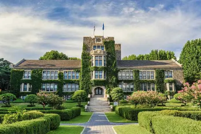 Historic ivy-covered building surrounded by neatly trimmed gardens and paths on a sunny day.