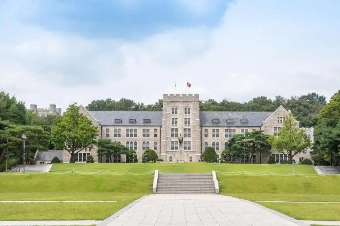 Front view of a historic stone building surrounded by greenery and trees, with a central staircase leading to the entrance.