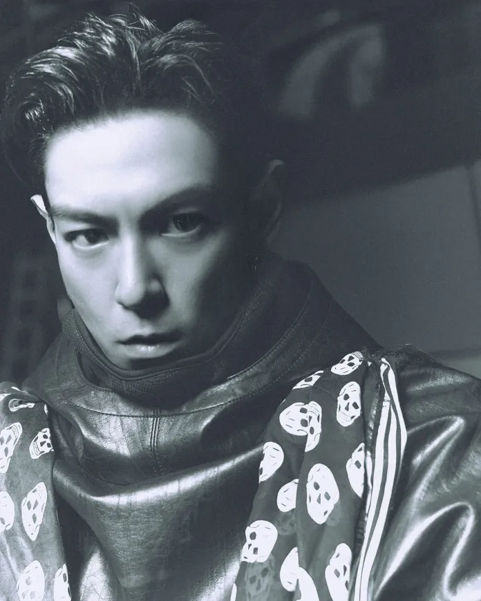 T.O.P with sleek, slicked-back hair wearing a leather jacket and a patterned scarf featuring skull designs, giving a serious expression.