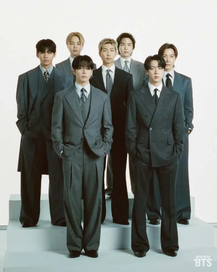 BTS members dressed in formal gray suits, standing together on a platform against a light-colored background.