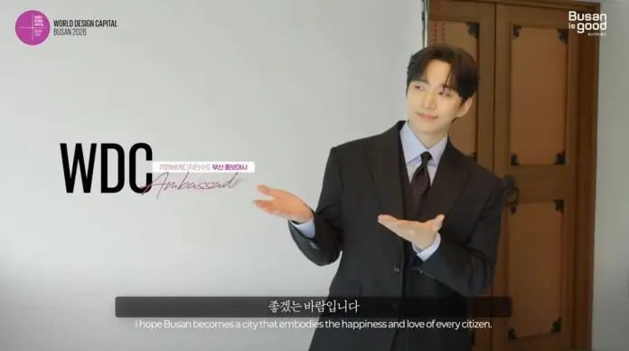 Lee Junho in a suit gestures with an inviting expression, promoting Busan as the World Design Capital 2028.