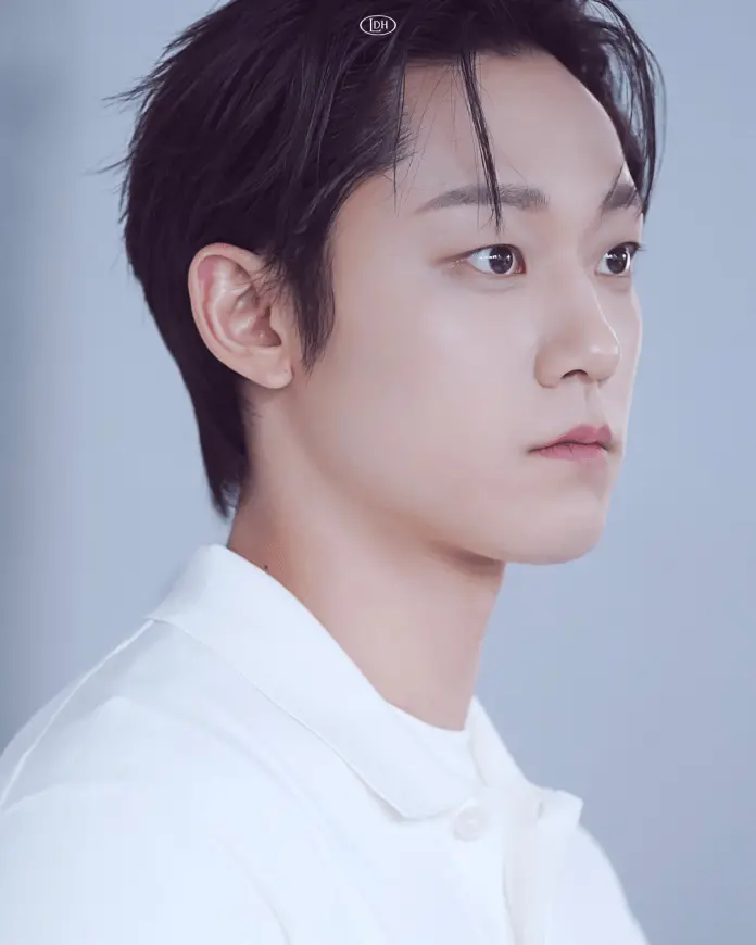 Profile portrait of Lee Do hyun with short dark hair, wearing a white collared shirt, set against a soft blue background.