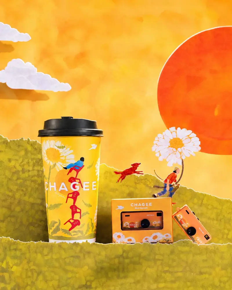 The CHAGEE Mini Digicam and a CHAGEE cup in a paper-craft scene with daisies, a red dog and a small figure