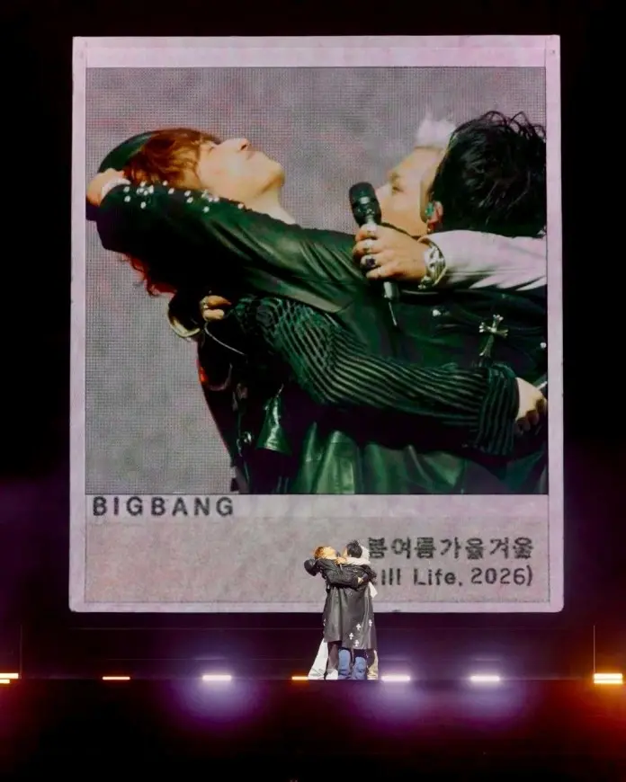 A performance by the K-pop group BIGBANG featuring G-Dragon, Taeyang and Desung embracing on stage with a large visual backdrop of a photo frame displaying their name and the title 'Full Life, 2026'.