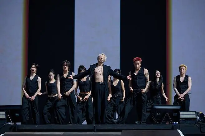 A group of performers in black outfits dancing on stage, with one central figure in a revealing top, showcasing a dynamic performance.