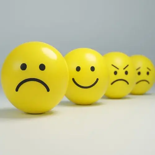 Cuatro esferas amarillas con rostros que muestran distintas emociones: tristeza, felicidad, enojo y confusión. Representan visualmente la inestabilidad emocional típica del trastorno bipolar. Fondo neutro, enfoque nítido y composición en línea.