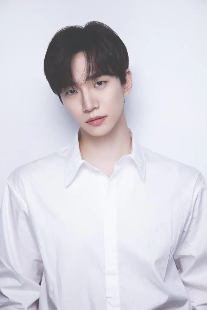 Lee Junho with short, dark hair wearing a white button-up shirt, standing against a plain white background.