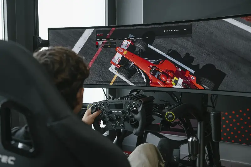 Gamer with Fanatec wheel controller playing Assetto Corsa EVO on ultrawide monitor, red Ferrari visible on screen