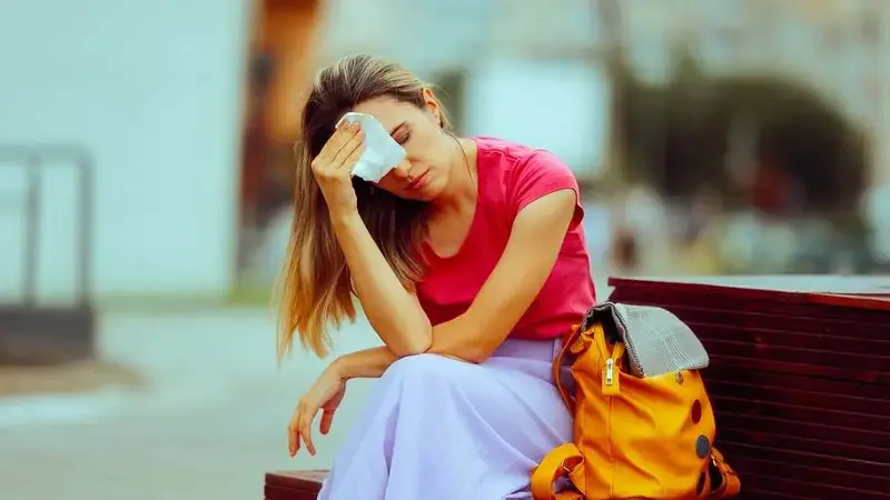 Woman sitting on bench looking tired and wiping forehead