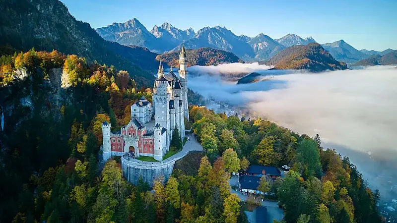 Neuschwanstein Castle amid autumn forests and misty bavarian alps from aerial view