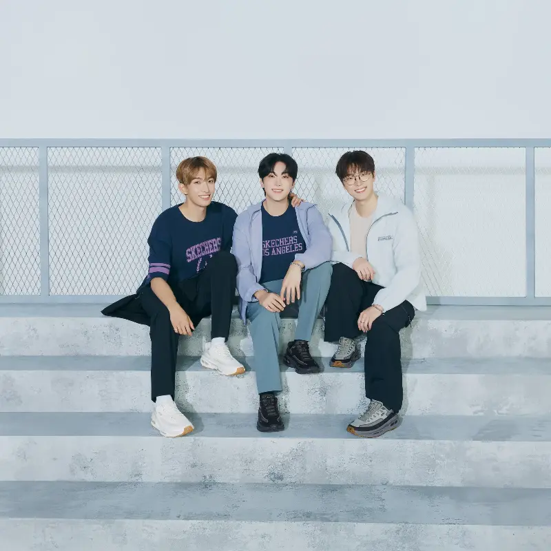 Members of SEVENTEEN sit on concrete steps wearing Skechers apparel and D'Lites 330 sneakers