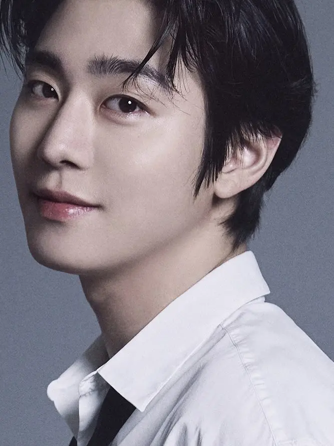 Close-up portrait of a young man with dark hair, wearing a white shirt, gazing slightly to the side with a soft expression against a neutral background.