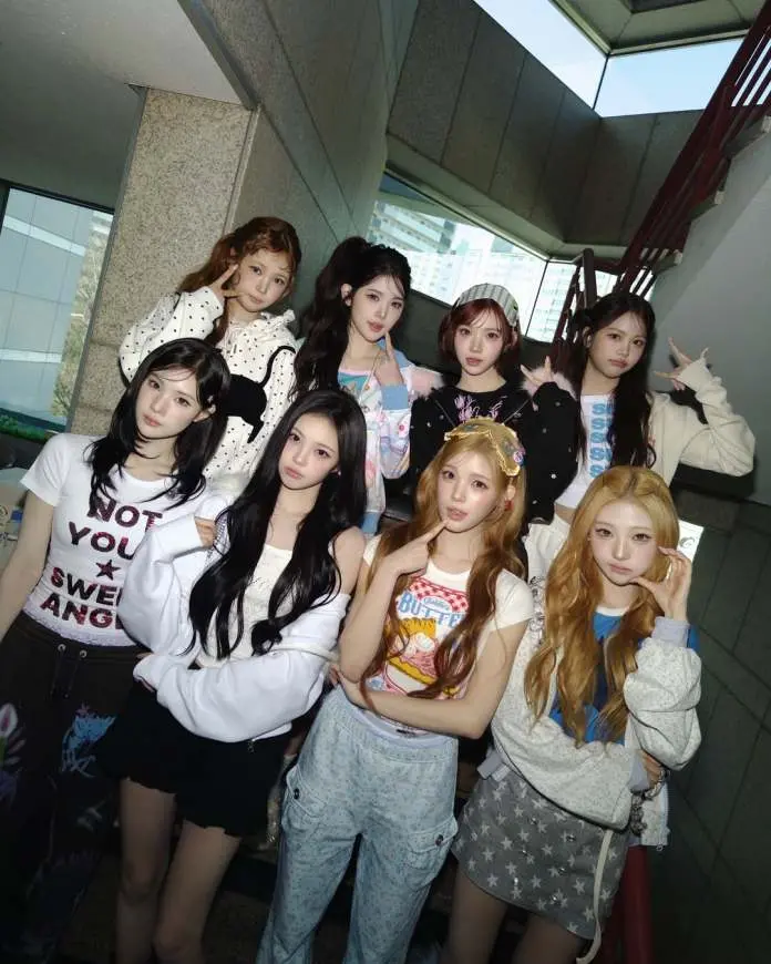 A group of nine young women posing together in a stairwell, wearing casual and stylish outfits. They are showing various expressions and gestures, with a mix of playful and serious poses.