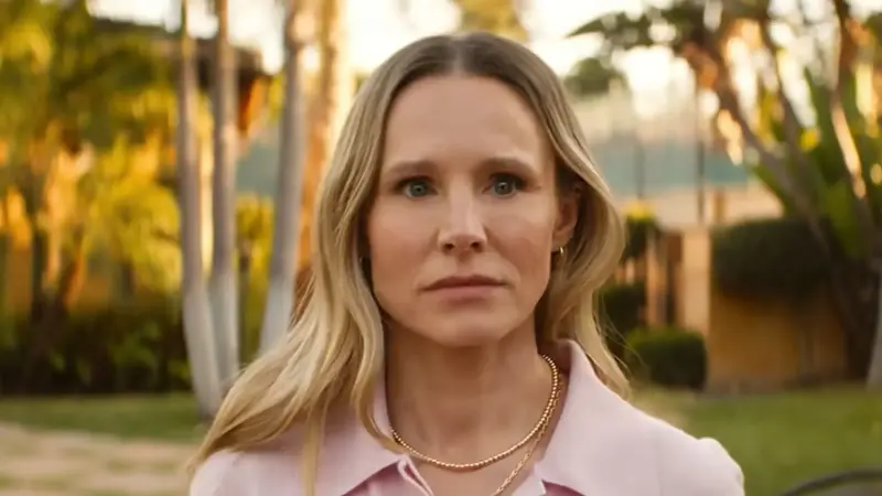 Kristen Bell looking stunned, wearing a pink shirt and standing in front of palm trees in Nobody Wants This Season 3.