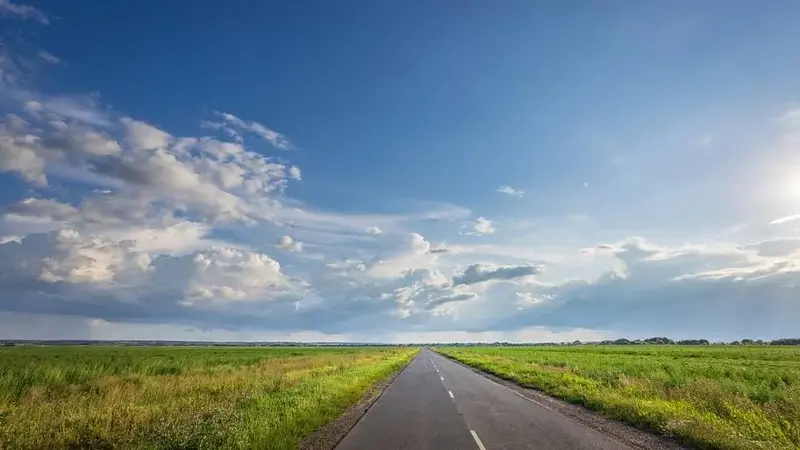 Blue cloudy sky above open country road
