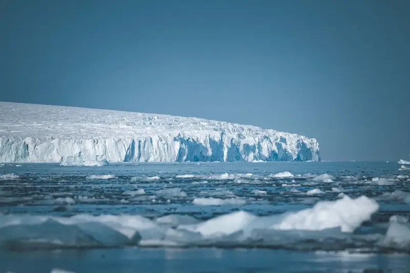 A vast icy landscape with towering icebergs and a serene, calm sea in Antarctica.