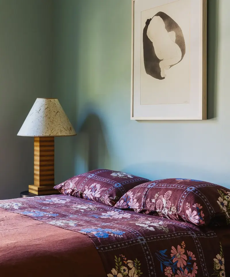 Sucher Studios warms cool blue walls with burgundy bedding, floral pattern, and striped wood, demonstrating how contrasting earthy tones prevent blue from feeling chilly. (Image credit: Sucher Studios)