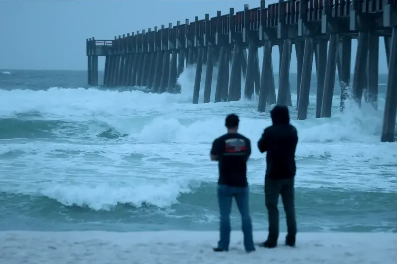 People look out at the waves churning in the ocean as Hurricane Isaias approaches on October 09, 2026, in Pensacola Beach, Florida.