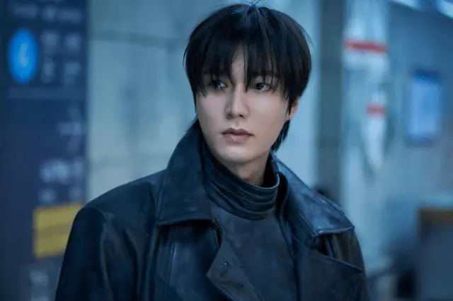 Close-up portrait of Lee Minho with dark hair wearing a black leather jacket, standing in an urban setting.