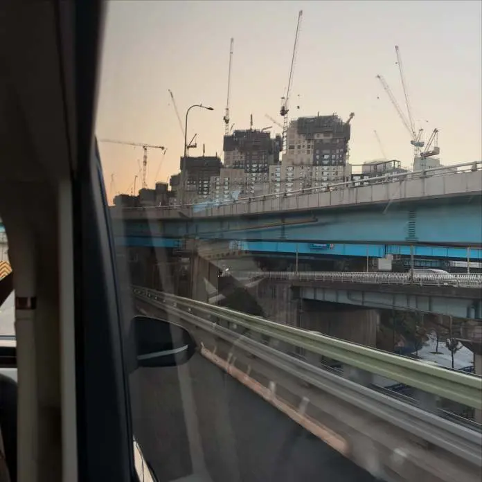 View from a vehicle showcasing a multi-level highway and construction cranes over buildings at sunset.