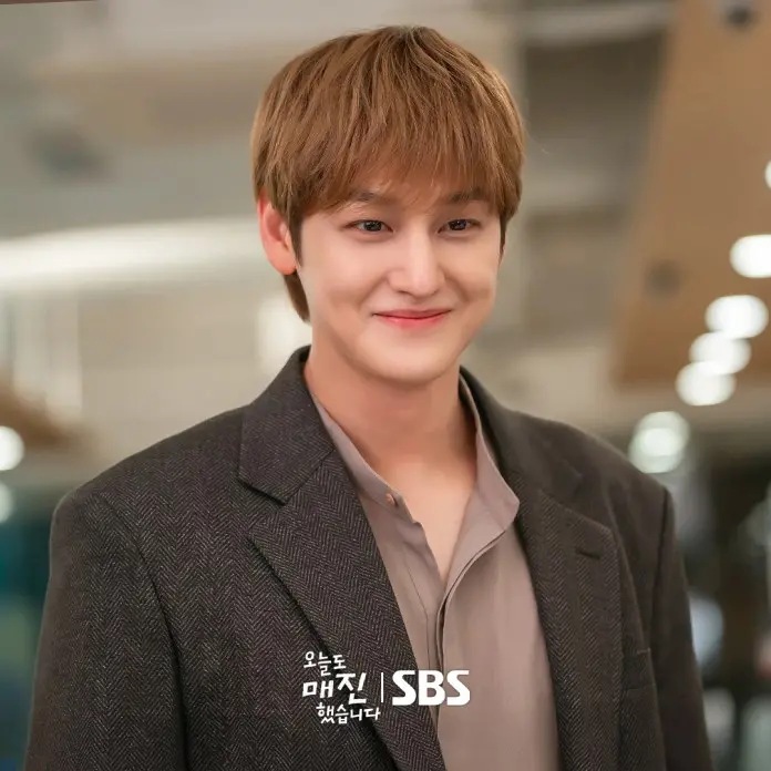 Kim Bum with light brown hair and a warm smile, wearing a grey blazer over a beige shirt, standing in a bright, modern interior.