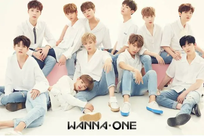 Wanna One posing together, dressed in white shirts and blue jeans, with a light background. The group is sitting and standing in various poses, showcasing a friendly and stylish appearance. The name 'Wanna One' is displayed at the bottom.